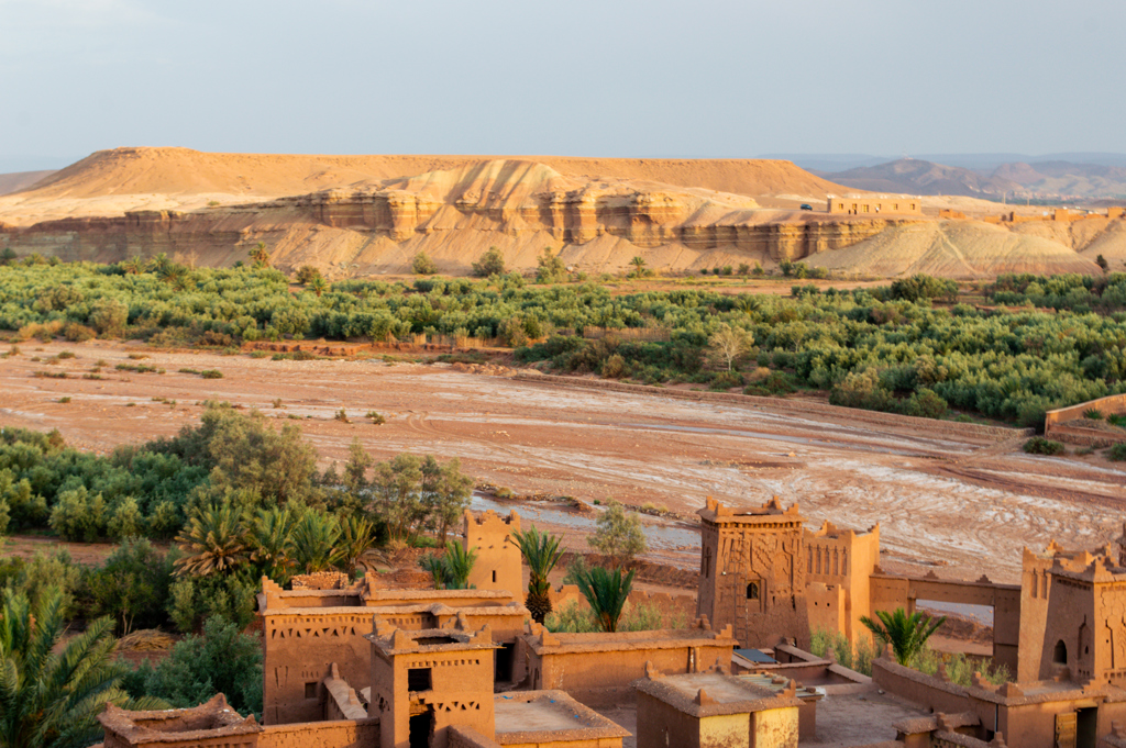 Leemkleurige kasbah aan een rivierbedding met palmoase en rotsplateau in Marokko tijdens een familiereis.