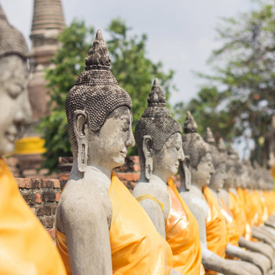 Rij boeddhabeelden met oranje gewaden bij een tempelcomplex in Thailand.