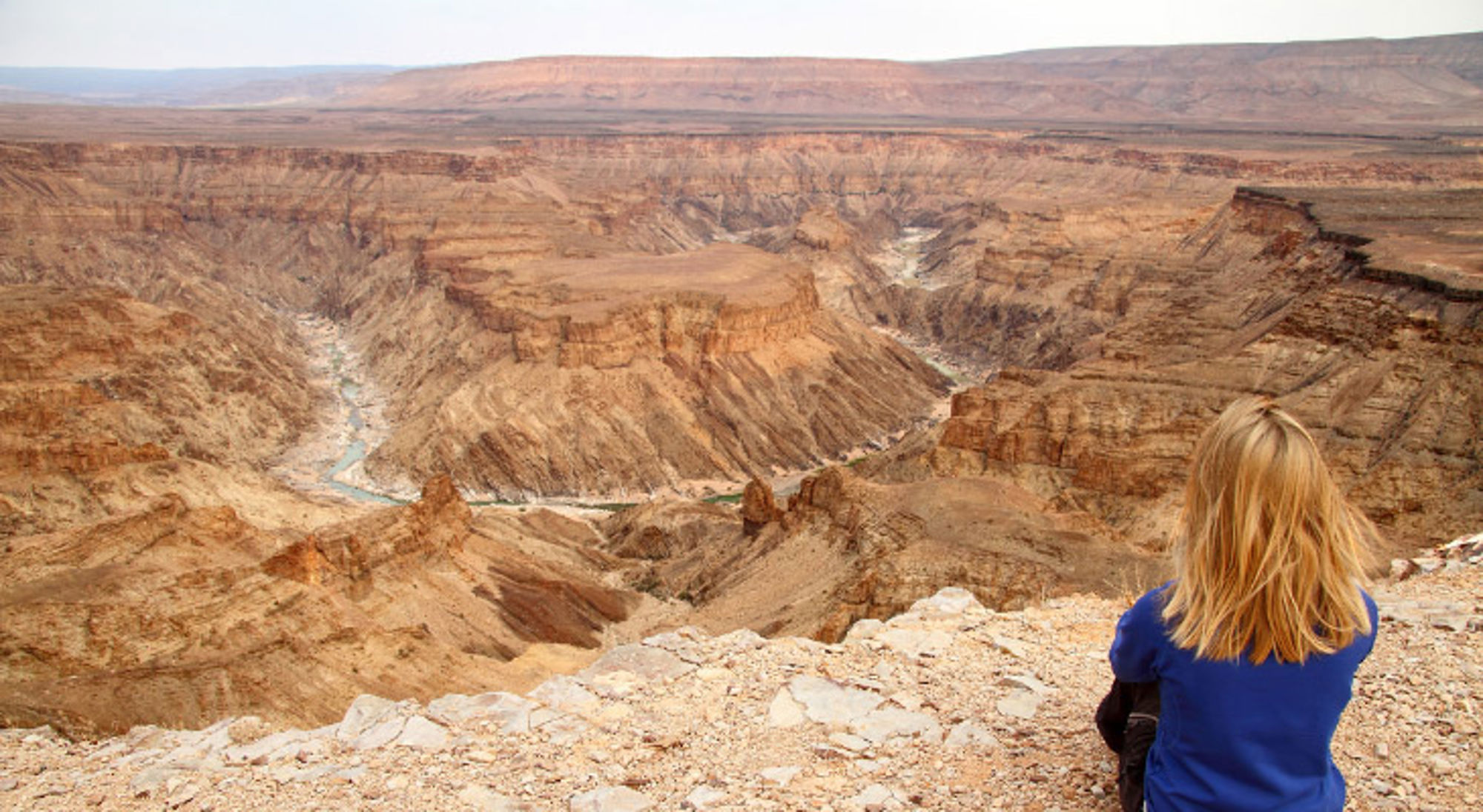 Uitzicht op de Fish River Canyon in Namibië, met een reiziger op een rotsrand.