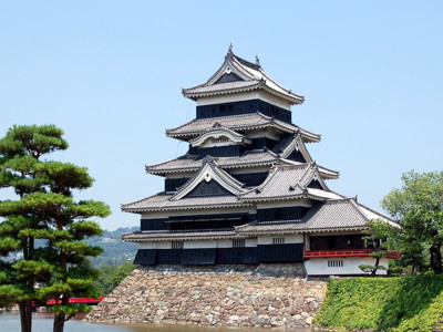Matsumoto-jo kasteel in Japan met zwarte houten gevels en gelaagde daken, omringd door water en groen.