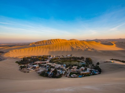 Huacachina-oase met lagune en dorp, omringd door zandduinen in Peru bij zonsondergang.