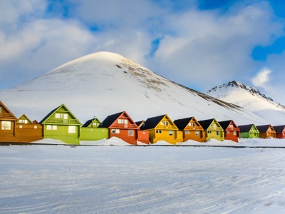 Gekleurde houten huizen in Longyearbyen op Spitsbergen, met besneeuwde bergen op de achtergrond.