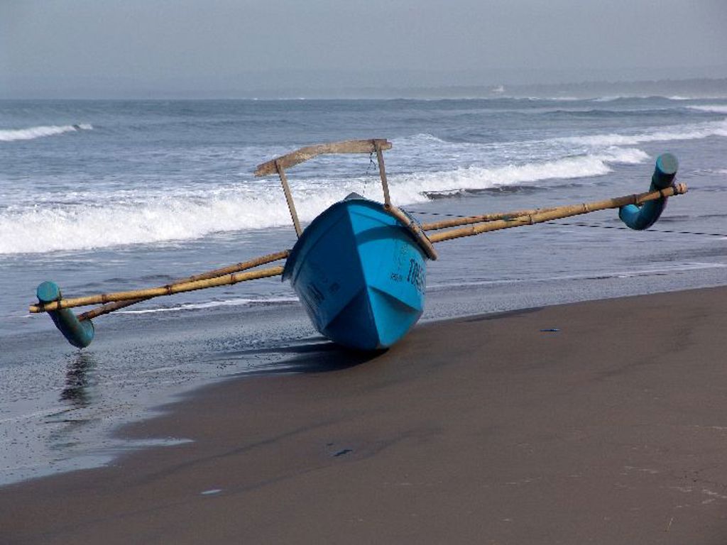 Blauwe vissersboot op het strand bij de branding op Bali tijdens een groepsrondreis Sumatra, Java en Bali.