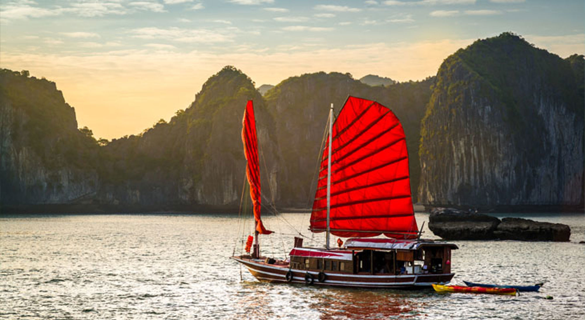 Traditionele boot met rode zeilen in Halong Bay, Vietnam, met kalkstenen rotsen op de achtergrond.
