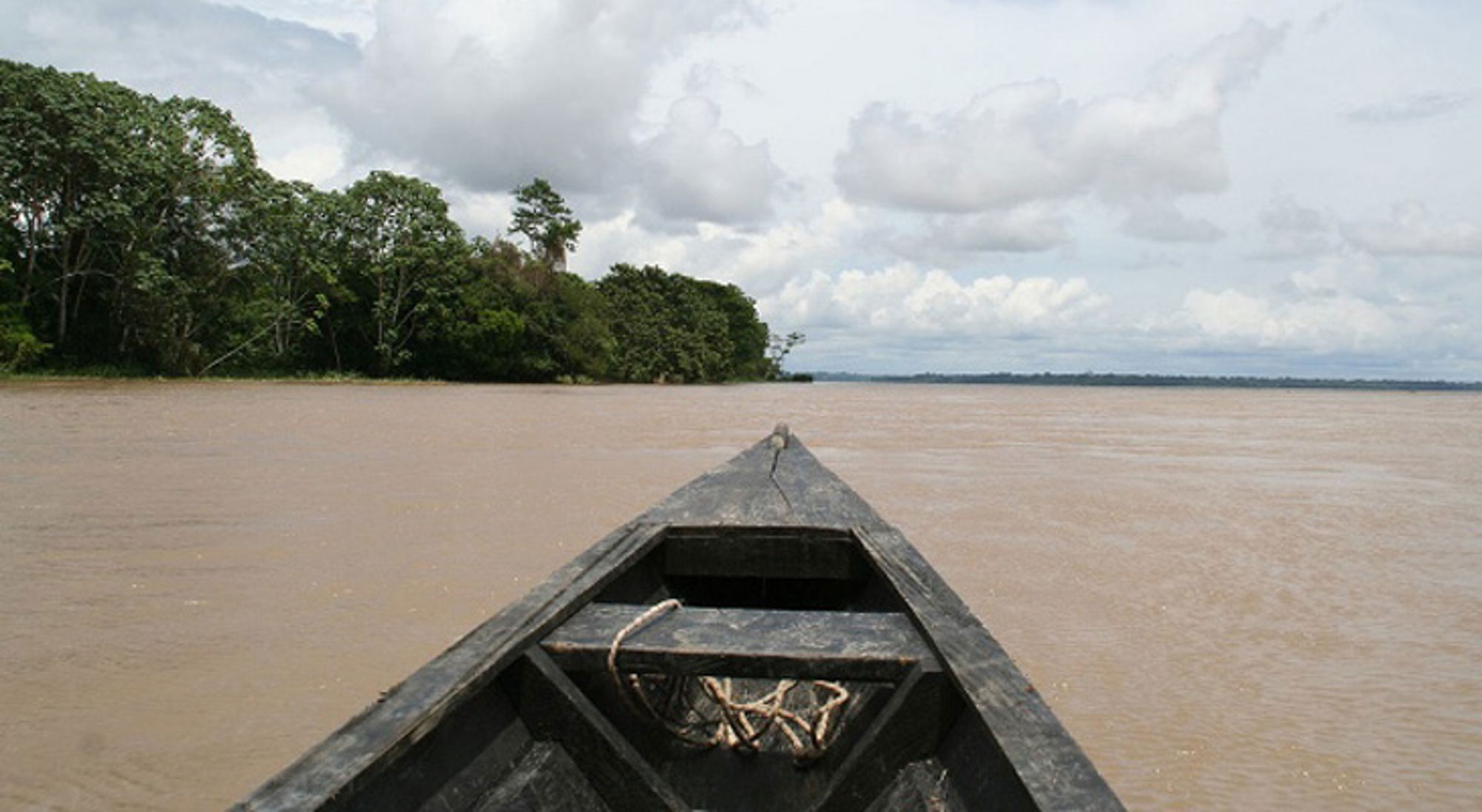 Houten kano op een brede rivier met regenwoud langs de oever in Colombia.