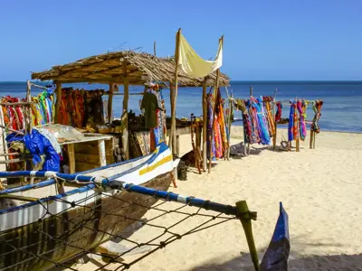 Strandmarkt op Madagascar met kleurrijke doeken, rieten kraam en vissersboot aan zee.
