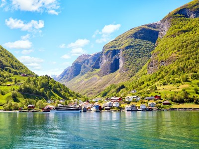Uitzicht op een Noors fjord met dorp aan de oever en groene bergen, route Scandinavië.
