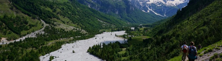 Wandelaars met rugzak in bergvallei in Albanië, met rivierbedding en groene hellingen.