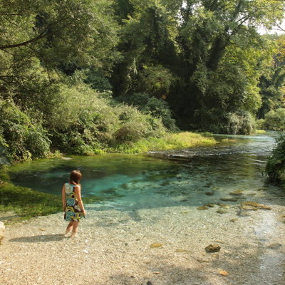 Vrouw bij helderblauwe rivier in groen boslandschap in Albanië.