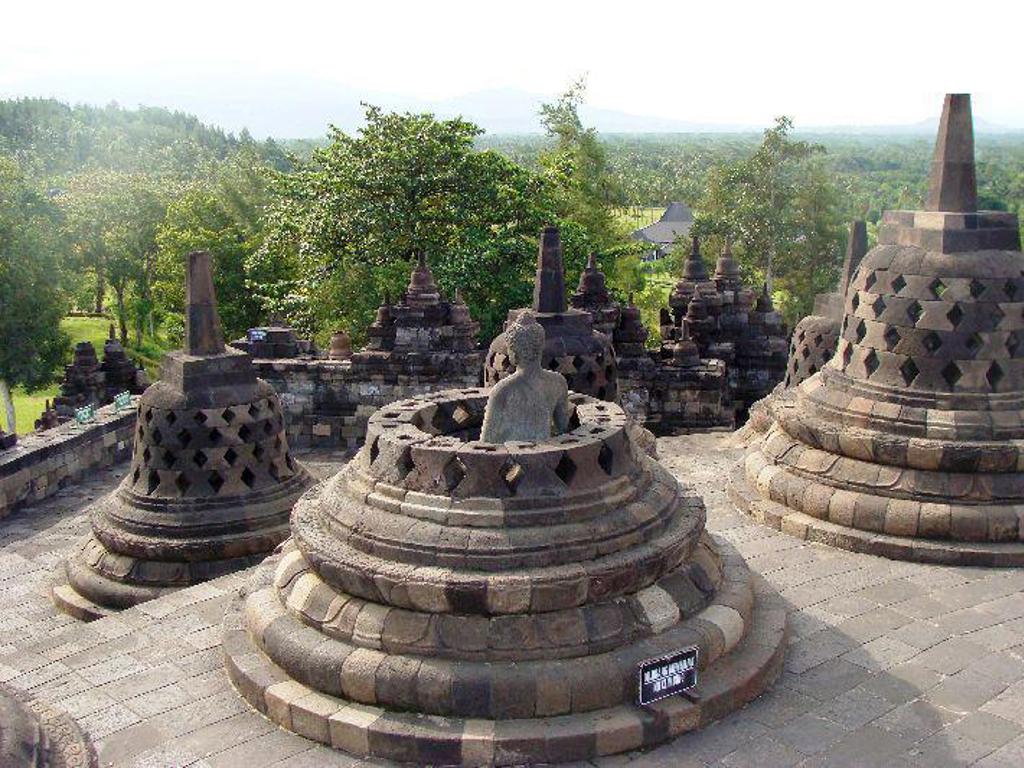 Stupa’s met boeddhabeeld bij Borobudur op Java, met groen landschap op de achtergrond.