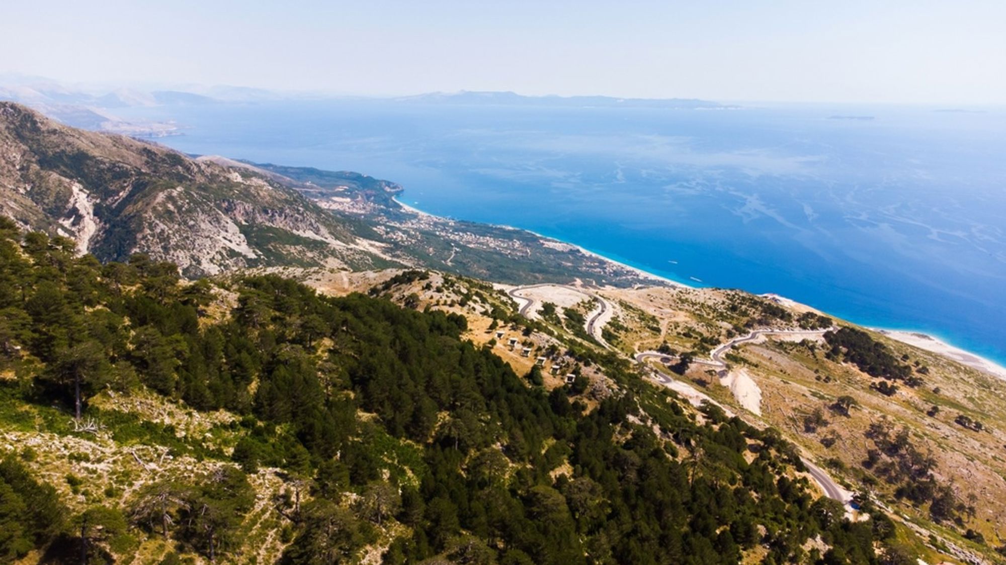 Panoramisch uitzicht op de Albanese Rivièra met bergweg langs de kust en het blauwe water van de Ionische Zee.