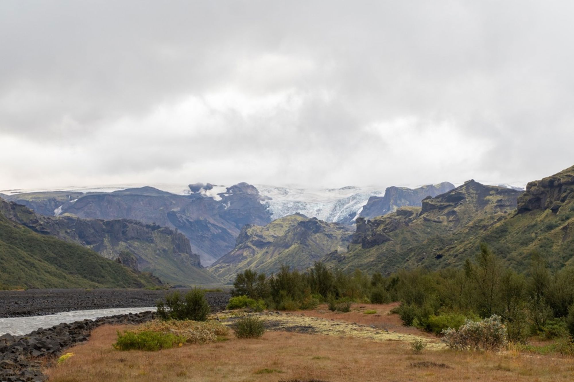 Berglandschap met gletsjer en rivier in IJsland onder een bewolkte lucht.