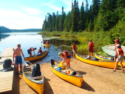 Kanotocht op een rustig meer in Canada, met reizigers die kano’s inladen bij de oever.