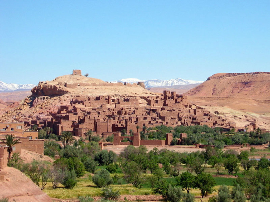 Kasbah Aït Ben Haddou in Marokko met palmoase en besneeuwde Atlasbergen op de achtergrond.