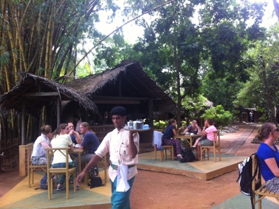 Lunchpauze op een openluchtrestaurant in Sri Lanka, met reizigers aan tafels en een ober met dienblad.
