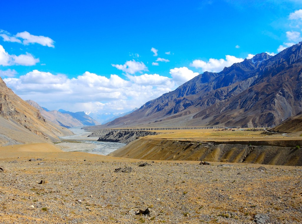 Berglandschap in Ladakh, India, met brede rivierbedding en hoge bergtoppen onder een blauwe lucht.