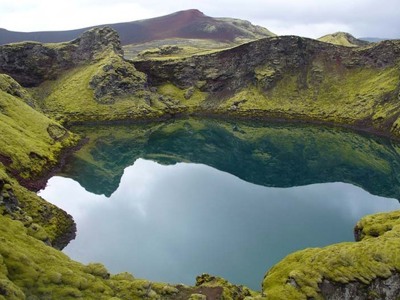 Kratermeer met helderblauw water, omringd door met mos begroeide lavavelden in IJsland.