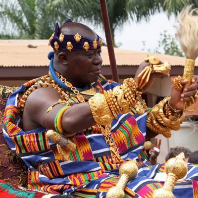 Traditionele ceremonie in Ghana met man in kleurrijke kente en gouden sieraden tijdens groepsrondreis Ghana, Togo en Benin.