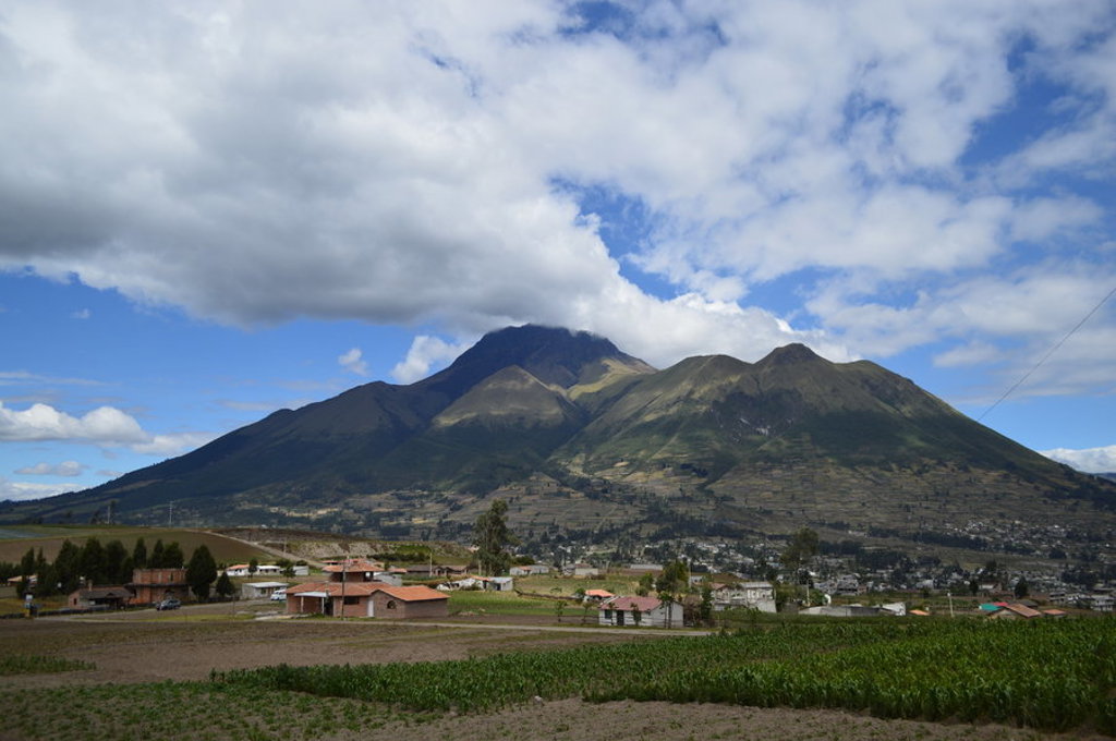 Groene vulkaanlandschap in Ecuador met dorp en akkers onder een wolkenlucht.