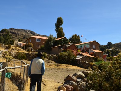 Wandelaar op een pad naar een dorp in de Andes met terrassen, stenen muurtjes en huizen onder een blauwe lucht.