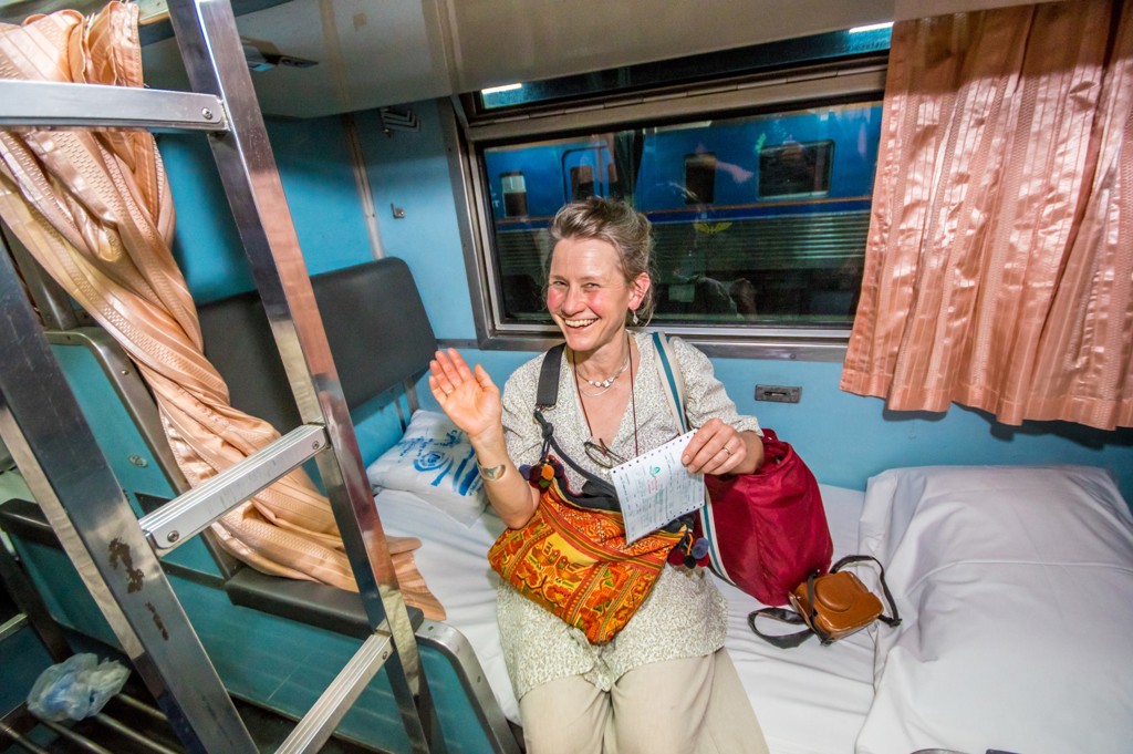 Reiziger in nachttrein in Thailand, zittend op een bed met ticket en bagage tijdens groepsrondreis.