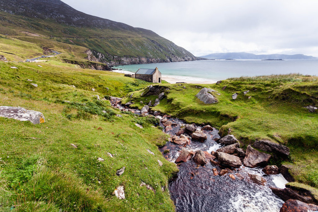 Groen kustlandschap met beekje, rotsen en een huisje aan een baai in Noord-Ierland en Ierland.