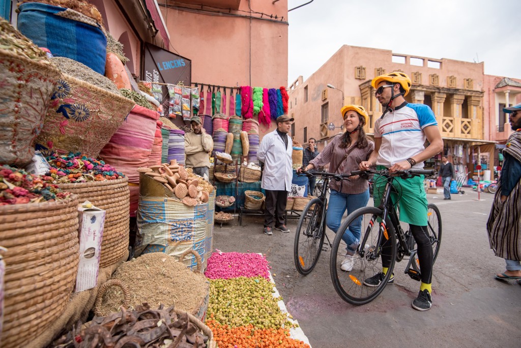 Fietsers op de markt in Marokko tussen kleurrijke kruiden en stoffen tijdens een fietsvakantie.