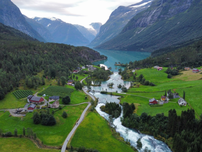 Groene vallei met boerderijen en rivier aan een fjord, omringd door bergen in Noorwegen.