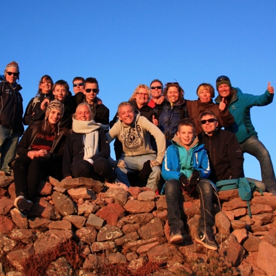 Familiegroep op een rotsachtige heuvel tijdens familiereis Peru, met duim omhoog bij zonsondergang.
