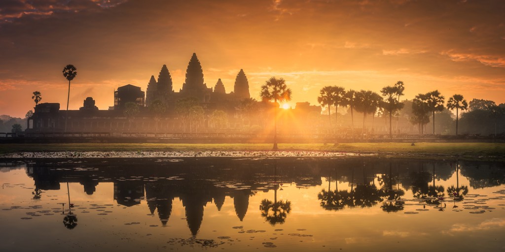 Zonsopkomst bij Angkor Wat met palmbomen en spiegeling in het water, Cambodja.