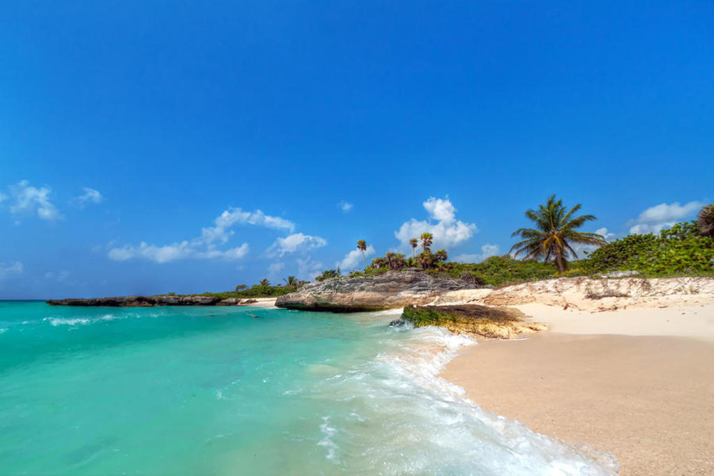 Tropisch strand in Mexico met turquoise zee, rotsen en palmbomen onder een blauwe lucht.
