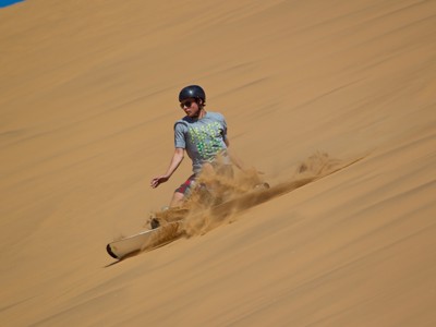 Sandboarden van een zandduin in Namibië tijdens de route Kaapstad–Victoria Falls.