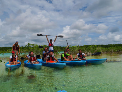 Groep reizigers in kajaks op een turquoise lagune met mangroven tijdens de Route Mexico.