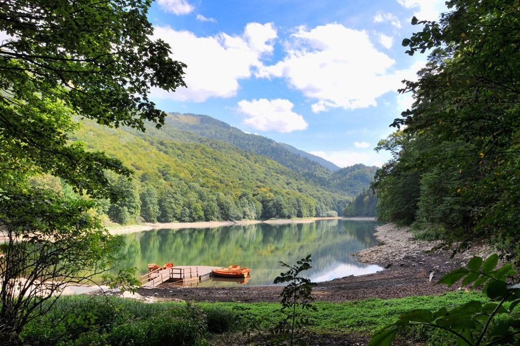 Bosmeer in de Balkan met bootjes aan een steiger, omringd door groene bergen en bos.
