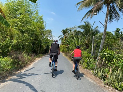 Fietstocht door de Mekongdelta in Vietnam, over een smalle weg langs palmen en tropisch groen.