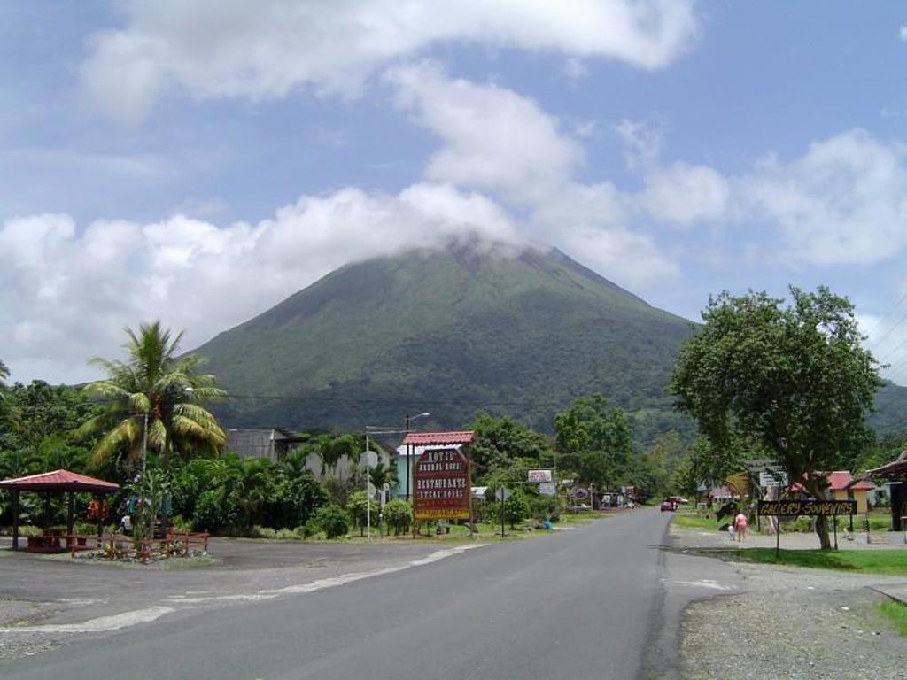 Groene vulkaan in Costa Rica gezien vanaf een weg met palmbomen en dorpje op de voorgrond.
