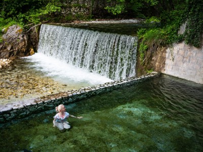 Vrouw baadt in helder rivierwater bij een kleine waterval in Noord-Griekenland.