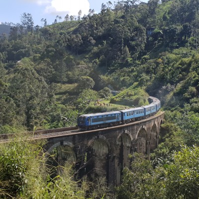 Blauwe trein op de Nine Arch Bridge tussen groene heuvels in Sri Lanka.