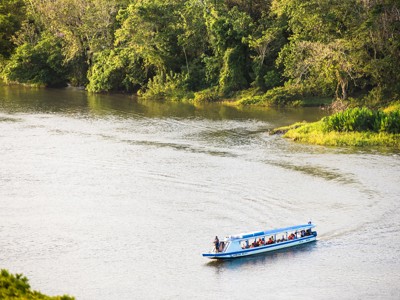 Boot met reizigers op een brede rivier langs dicht regenwoud in Costa Rica en Nicaragua.