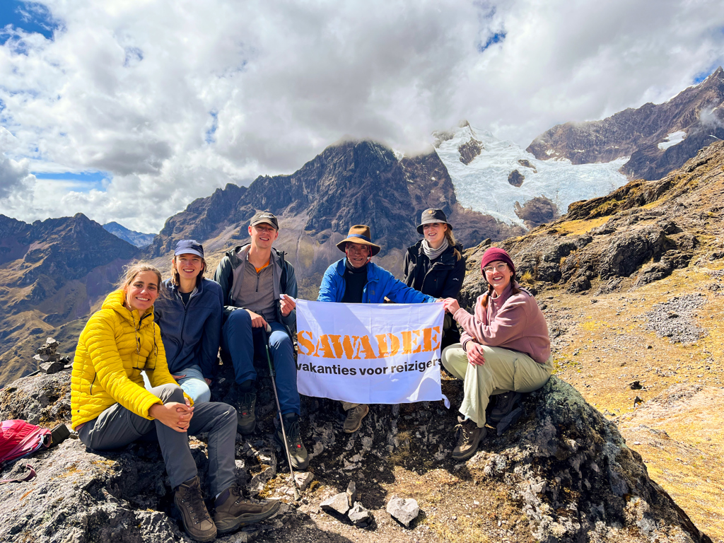 Groep 22-35ers wandelaars in de Peruaanse Andes met Sawadee-vlag, met besneeuwde bergtoppen op de achtergrond.