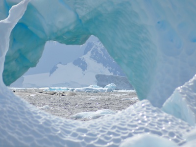 Blik door een ijsboog op drijvend pakijs en besneeuwde bergen in Antarctica.