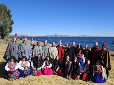 Groepsfoto bij het Titicacameer in Peru, met reizigers in kleurrijke kleding en mutsen aan de oever.