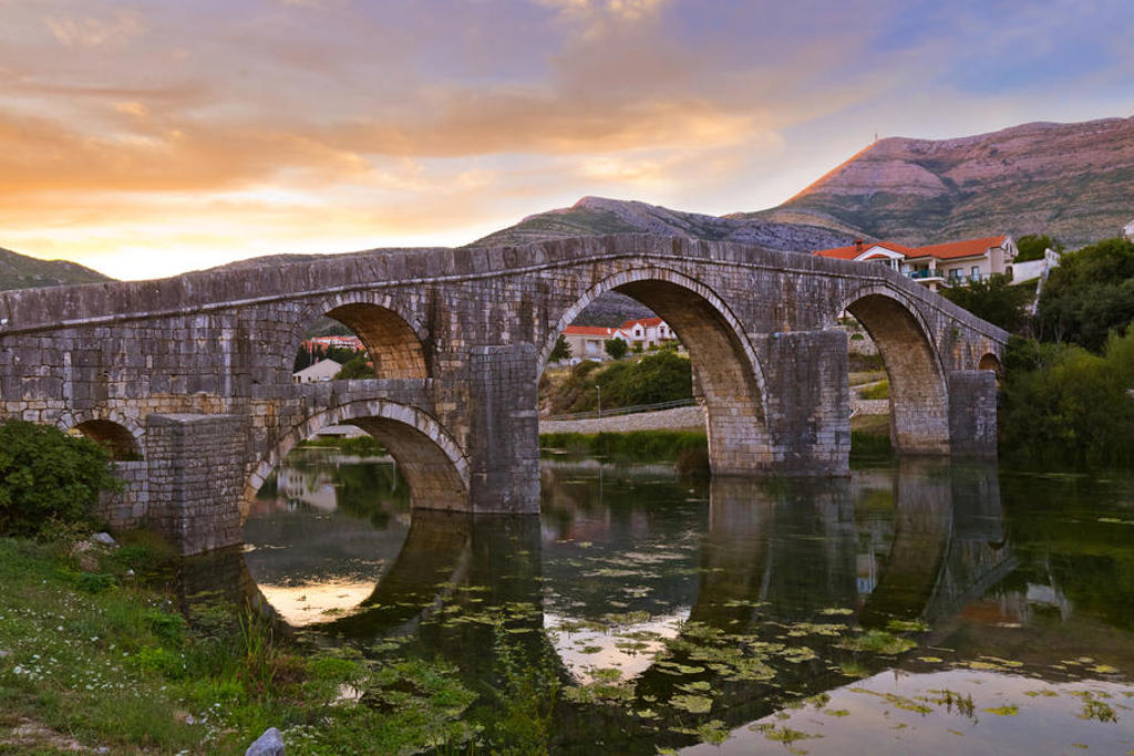 Oude stenen boogbrug over een rustige rivier in Montenegro bij zonsondergang tijdens een 22-35ers reis Balkan.