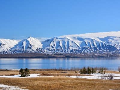 Besneeuwde bergen aan een fjord in Noord-IJsland onder een strakblauwe lucht.