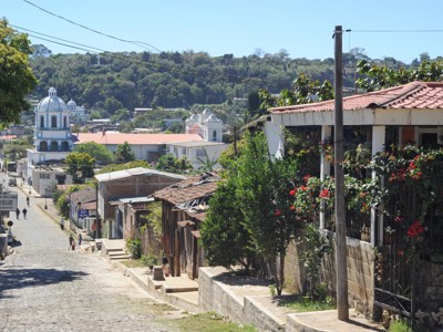 Straat in Copán Ruinas met uitzicht op de blauw-witte kerk en groene heuvels in Honduras.