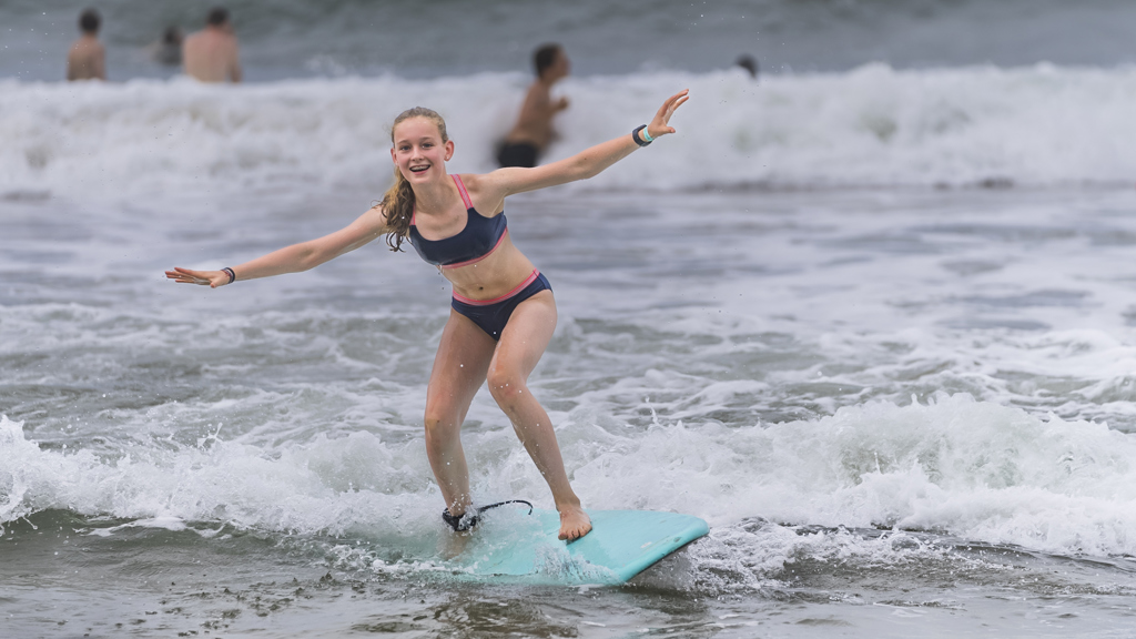Kind surft op een golf aan het strand tijdens een familiereis in Costa Rica.