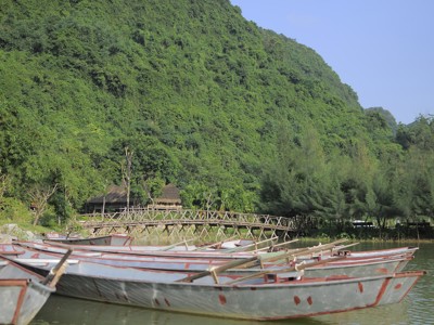 Roeiboten aan de oever bij een houten brug in het groene landschap van Vietnam tijdens de Route Vietnam.