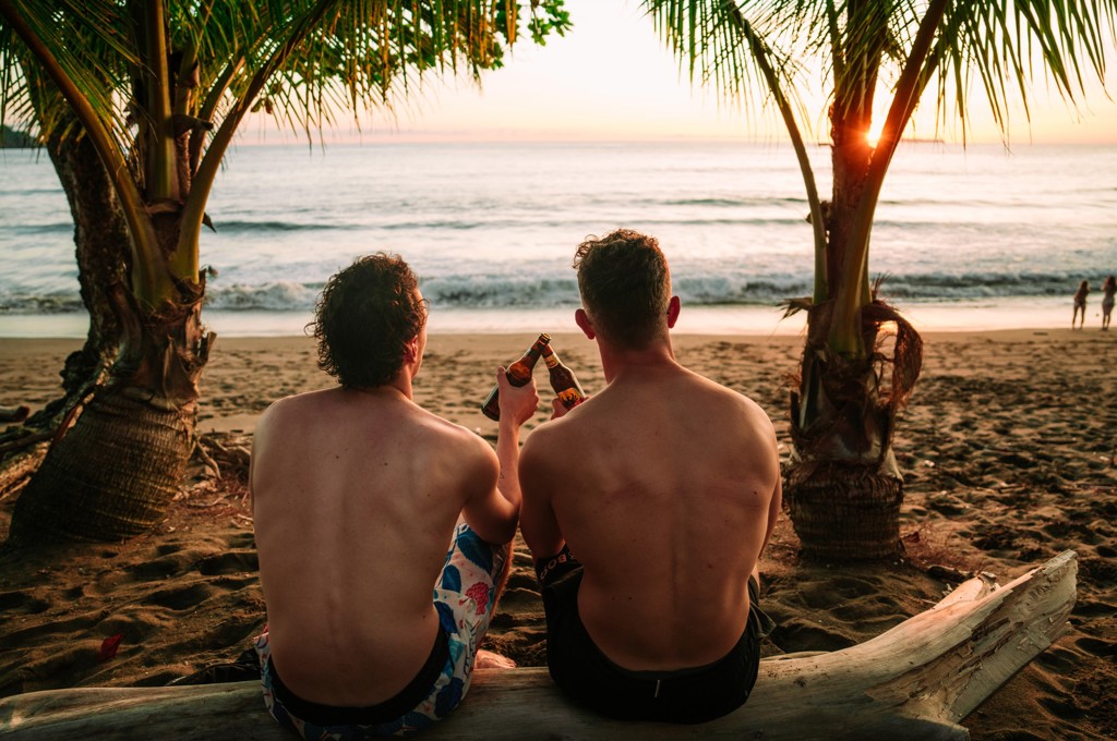 Twee reizigers proosten bij zonsondergang op het strand in Costa Rica, omringd door palmbomen.