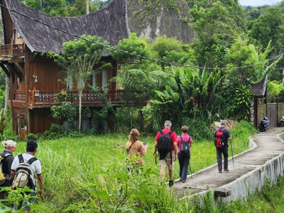 Wandelaars lopen door het groene landschap langs traditionele huizen op Sumatra tijdens de route Sumatra, Java en Bali.