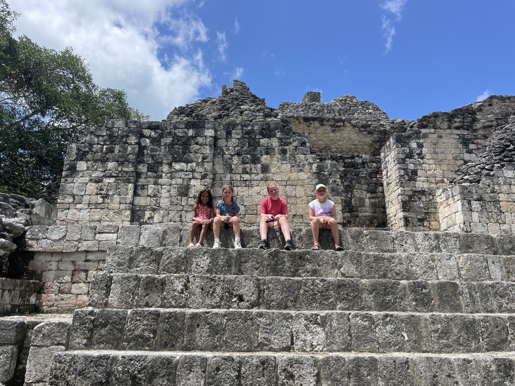 Kinderen zitten op de trappen van een oude Maya-piramide in de jungle tijdens een familiereis Mexico.